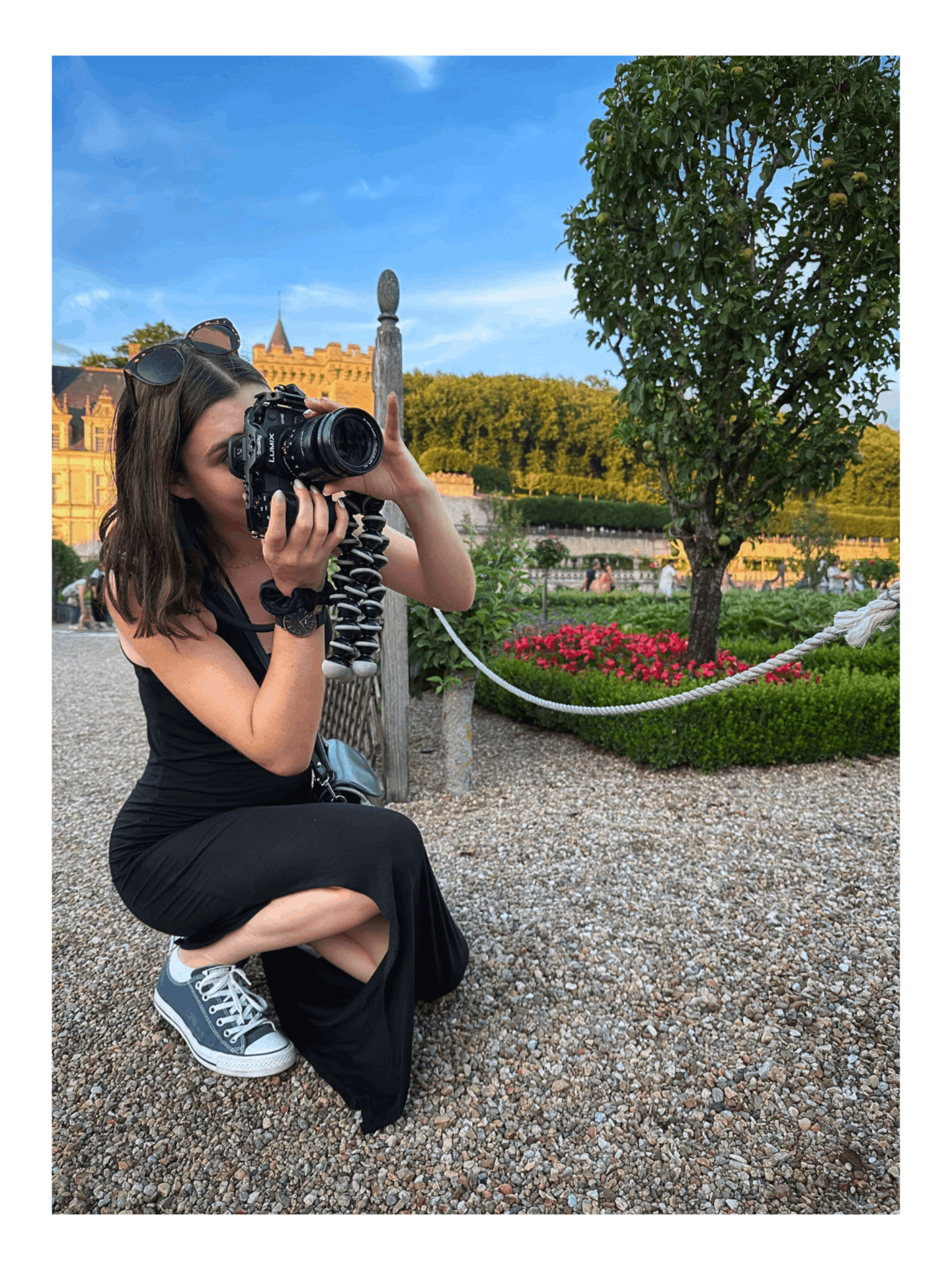 Vidéaste professionnelle accroupie en tenue sombre captant discrètement un instant sur le vif avec son boîtier hybride Lumix dans les allées d'un domaine.